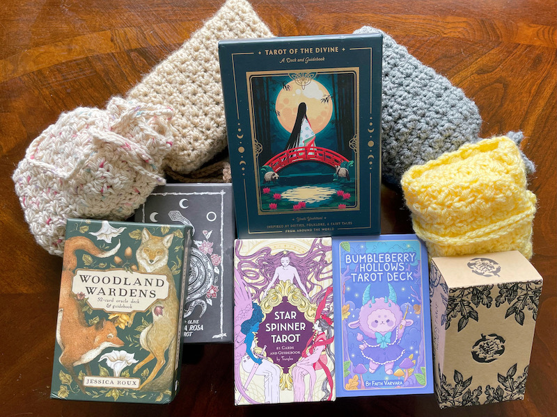 photo of my tarot decks piled on a coffee table, including some in handmade crochet bags